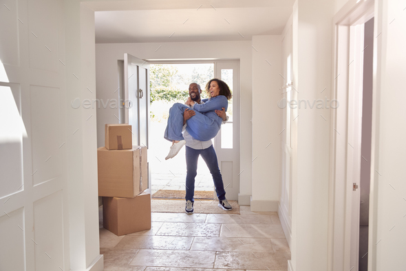 Man Carrying Woman Over Threshold As Couple Stand In Hallway Of New Home On Moving Day
