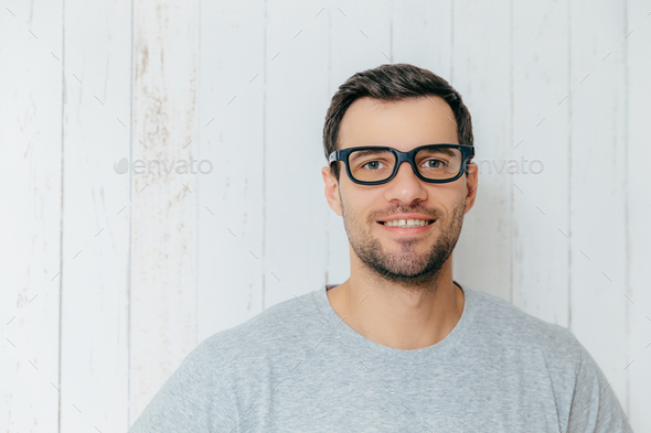 Handsome male with dark hair, wears spectacles, has gentle smile, looks directly into camera - Stock Photo - Images
