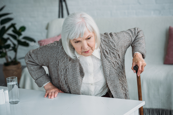 portrait of grey hair woman with walking stick trying to get up at home