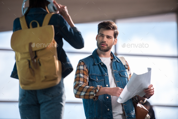 stylish male traveler with map in hand asking for help woman with headphones and backpack at subway