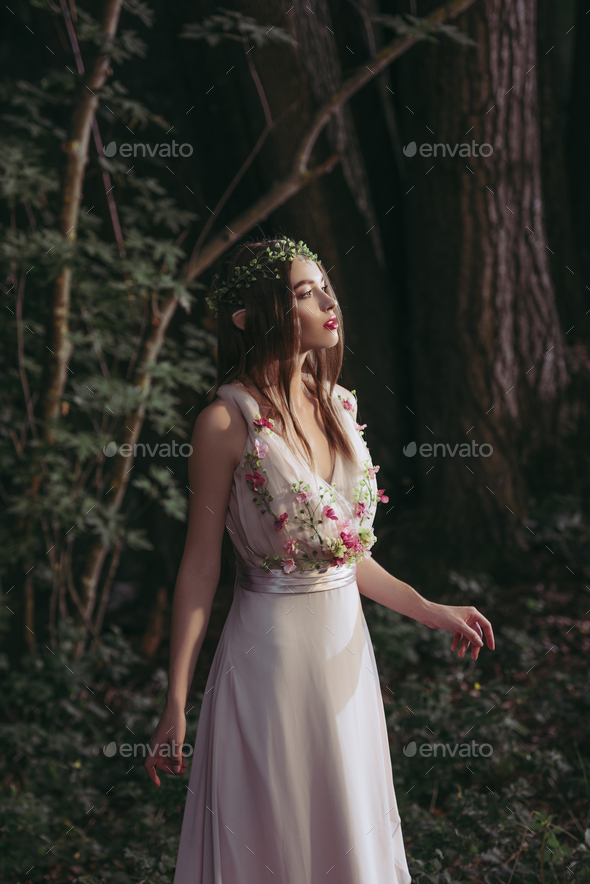 attractive mystic elf in dress with flowers in dark woods