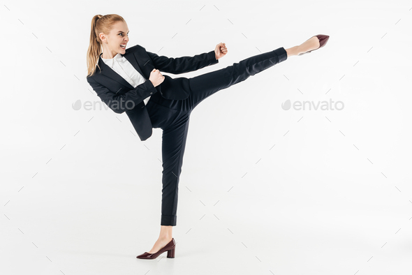 businesswoman performing karate kick in suit and high heels isolated on white