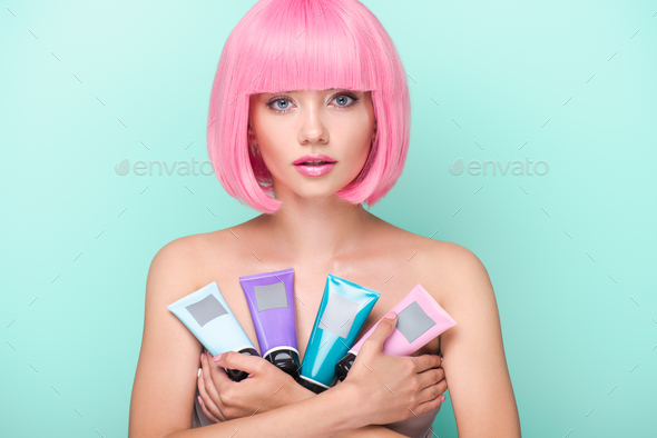 beautiful young woman with pink bob cut holding various tubes of coloring hair tonics looking at