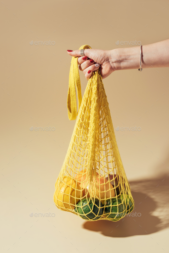 partial view of person holding string bag with fresh tropical fruits on brown