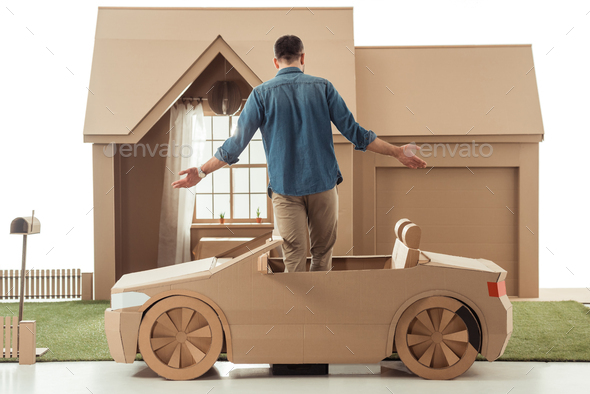 rear view of man in cardboard car in front of cardboard house isolated on white