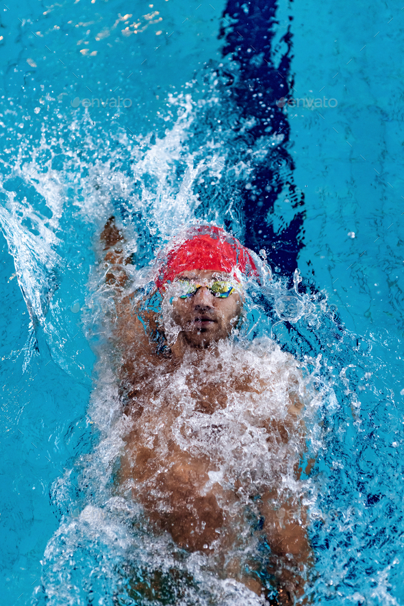 Top view of professional male swimmer in red swimming cap and goggles practicing and training at