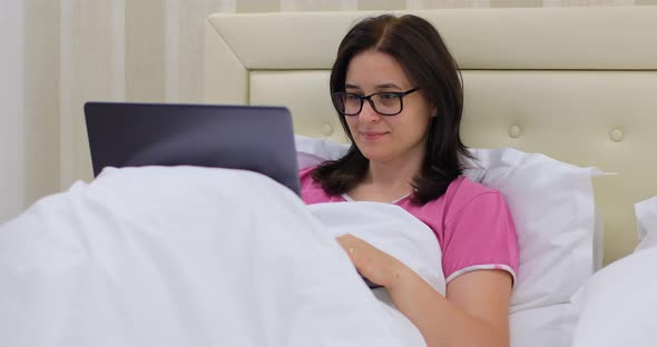Woman with Glasses Working on Laptop Computer in Bed