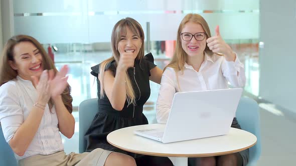Business girls in the office look at the laptop, rejoice and look at the camera