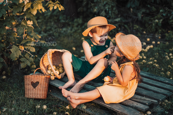 Children in overalls and straw hats eat pear while sitting on pallet