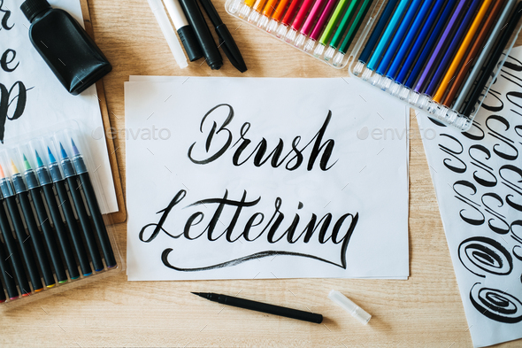 Brush Lettering text on paper and brushes and colored pencils on the table. Lettering art and