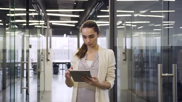 Business Lady Revisioning Information on Her Tablet PC while Standing in Long Office Hall alt