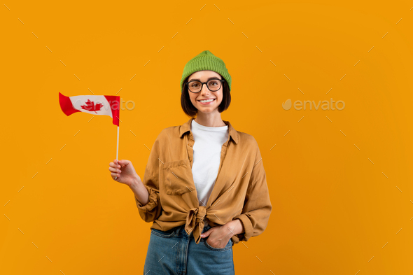 Modern foreign education concept. Happy female exchange student holding small flag of Canada, yellow