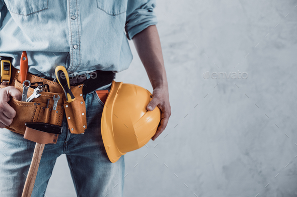 Worker man holding construction helmet tool near concrete or cement wall. Male hand and hard hat - Stock Photo - Images