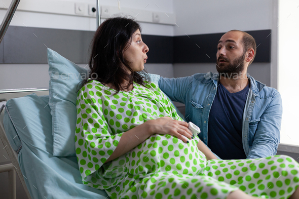 Young couple with pregnancy sitting in hospital ward bed
