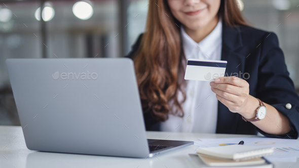 An asian businesswoman holding credit cards while using laptop computer in office - Stock Photo - Images