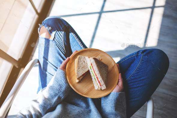 a woman holding two pieces of whole wheat sandwich in wooden plate while sitting on the floor