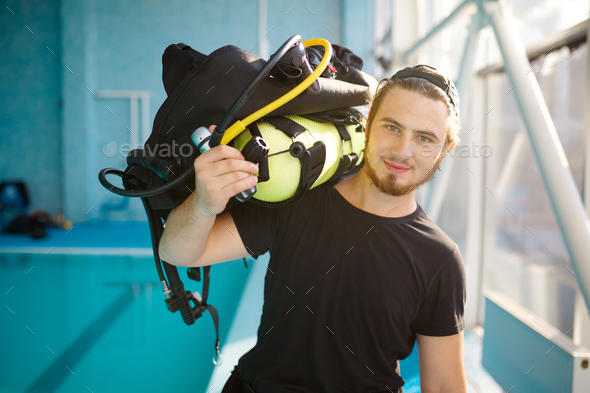 Male diver holds scuba gear, diving school