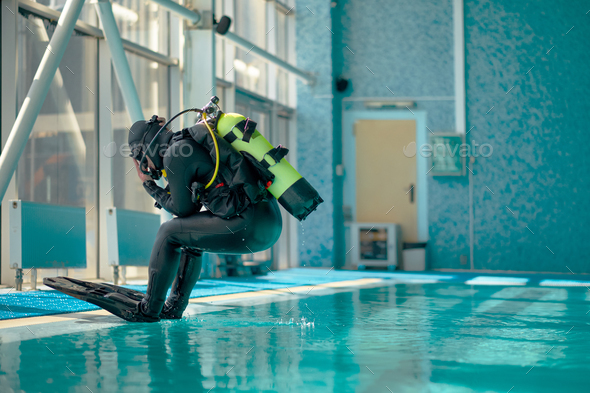 Male diver in scuba gear jumps into the pool