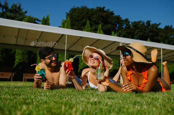 Cheerful friends rest on the grass near the pool - Stock Photo - Images