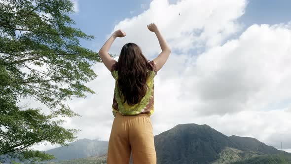 Girl with Long Hair in a Colored Tshirt and Yellow Trousers Stands and Raises Her Hands Up Against alt