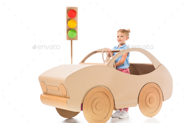 stylish female preschooler driving cardboard car on white with traffic lights