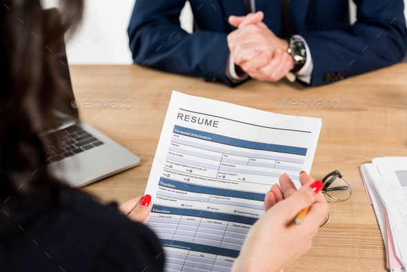 cropped view of recruiter holding resume near employee with clenched hands