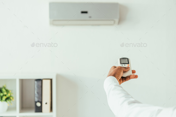 cropped view of african american businessman holding air conditioner remote controller in office
