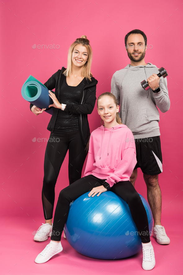 happy sportive family with fit ball, fitness mat and dumbbell isolated on pink