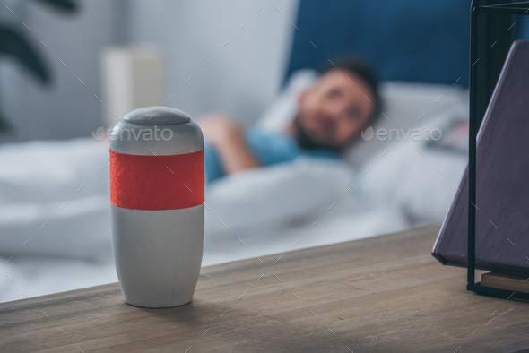 selective focus of funeral urn with man lying in bed on background