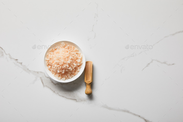 See salt wih with dried flower petals in wooden scoop on pink marble table, Stock image