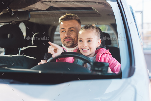 Daughter sitting in car with dad and pointing at car window