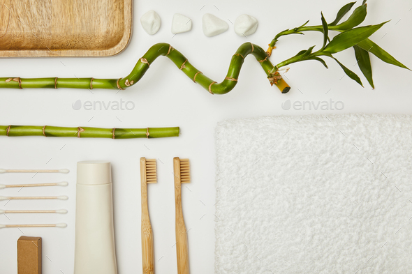 top view of towel, ear sticks, toothpaste in tube, cosmetic cream, toothbrushes, stones and bamboo