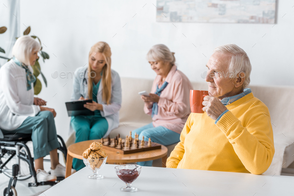 senior man drinking tea while doctor examining senior women