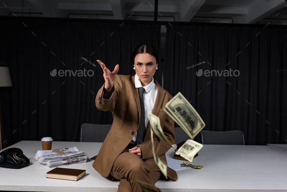 businesswoman sitting on table, throwing money and looking at camera