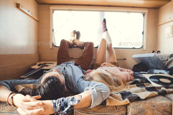 hippie couple lying inside campervan with acoustic guitar and vinyl player
