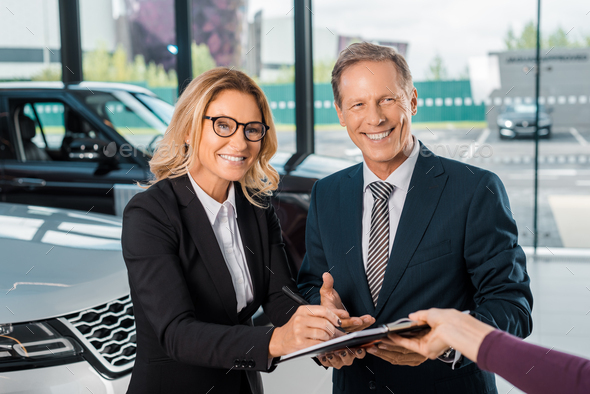 happy business couple signing papers for buying new car in showroom