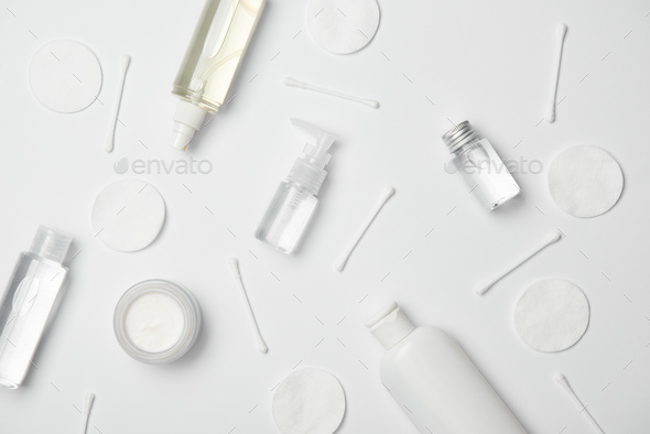 Top view of different cosmetic containers, cotton sticks and cosmetic pads on white background
