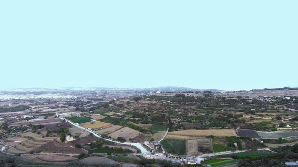 Aerial drone footage flying towards the Verdala Palace with patchwork countryside below of fields fo alt