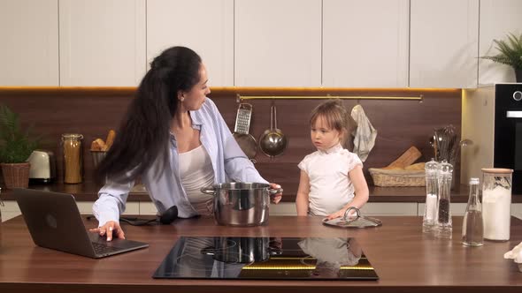 Attractive Mother and Her Daughter Cook in the Kitchen Looking Recipe in a Laptop alt