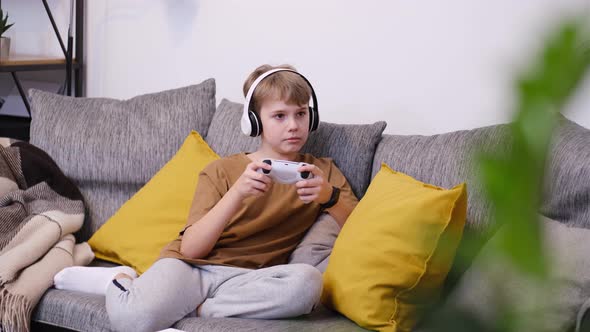 Boy Teenager Playing Video Game with Joystick Sitting on Sofa alt