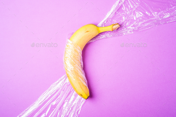 Banana fruit wrapped in stretch wrap plastic on pink background