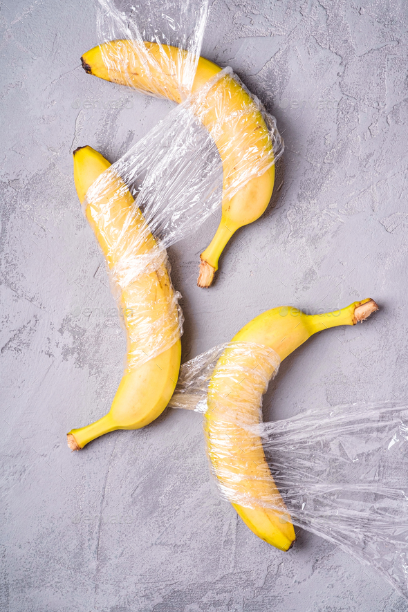Banana fruit wrapped in stretch wrap plastic on stone concrete background