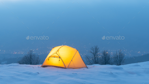 Yellow tent lighted from the inside against the backdrop of glowing city lights - Stock Photo - Images
