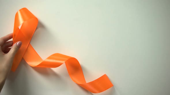 Female Placing Orange Ribbon on Table, Leukemia Awareness Campaign, Precaution alt