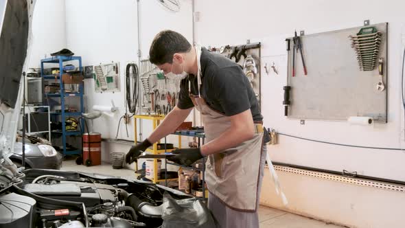 Male car mechanic wearing protective mask performs safety checklist on the car engine, in an auto re alt