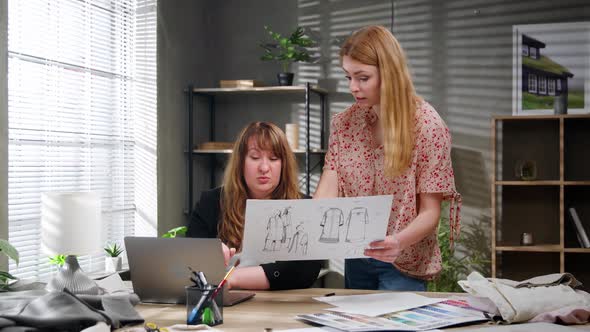 Two Young Businesswomen Discuss New Clothing Models for Their Studio alt