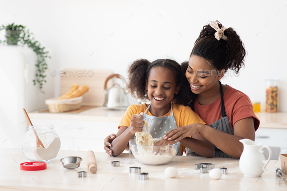 Afro-american mother showing her teen kid how to bake cookies