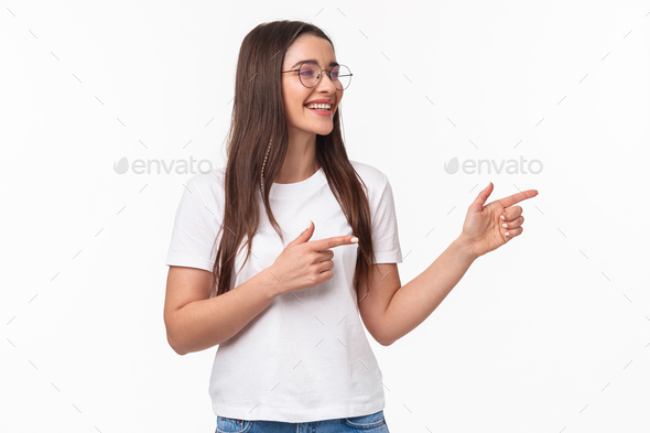 Waist-up portrait of cheerful young female student, programmer, pointing fingers and looking at
