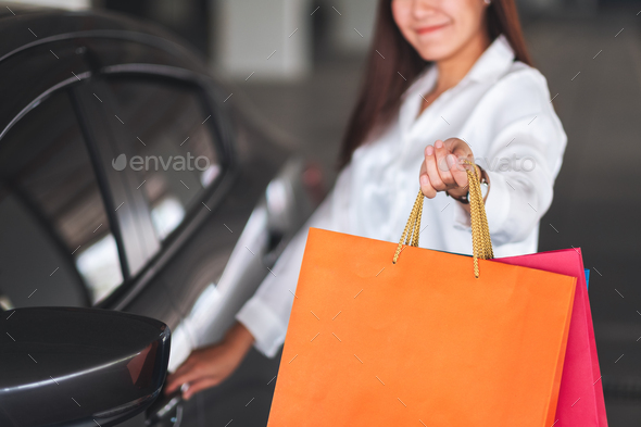 a beautiful woman holding and showing shopping bags while opening car door in the mall parking lot