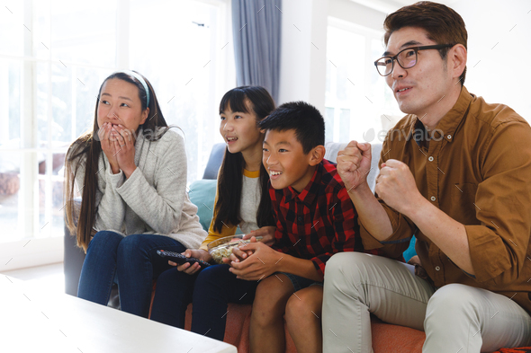 Smiling asian parents with son and daughter sitting on couch watching tv with popcorn - Stock Photo - Images